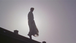 Man in white robe walking on an edge with sun behind him, unable to makeout a face.