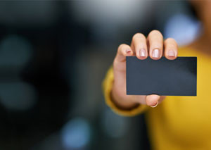 Blank black business card held up by woman who is blurred in the background.