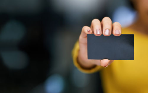 logos Blank black business card held up by woman who is blurred in the background.