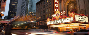 Outside brightly lit Chicago theatre, cars passing by.