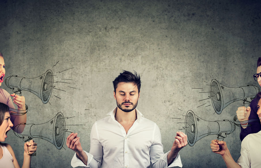 Young business man meditates while people shout at him with illustrated megaphones.