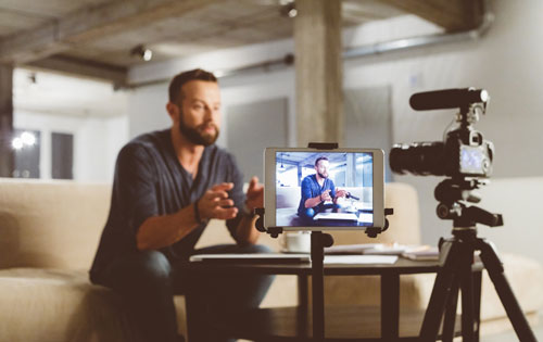 Young man seated at a couch talks to a video camera.