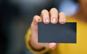 Close-up of blank black business card behind held up by woman who is blurred in foreground.