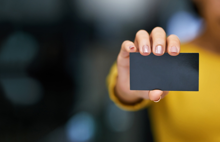 Close-up of blank black business card behind held up by woman who is blurred in foreground.