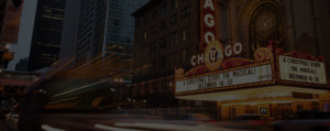 Outside brightly lit Chicago theatre with cars passing by.
